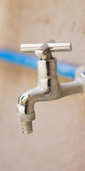 A close-up view of a shiny stainless steel faucet attached to a blue pipe on a wall.